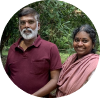 A smiling couple posing outdoors with green trees in the background.