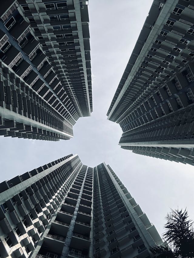 A low-angle view of four modern high-rise buildings converging towards the sky, creating a geometric perspective.