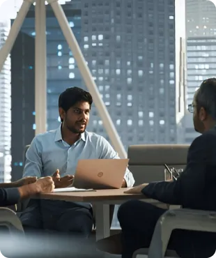 Two business professionals engaged in a discussion at a modern office setting with large windows and cityscape in the background.