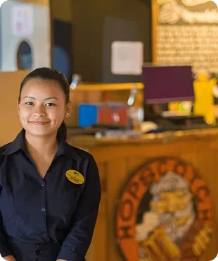 Smiling woman in a professional uniform standing at a reception desk in a warmly lit environment.