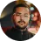 Circular profile image of a man with a beard, wearing a dark outfit, in a dimly lit setting with a blurred background.